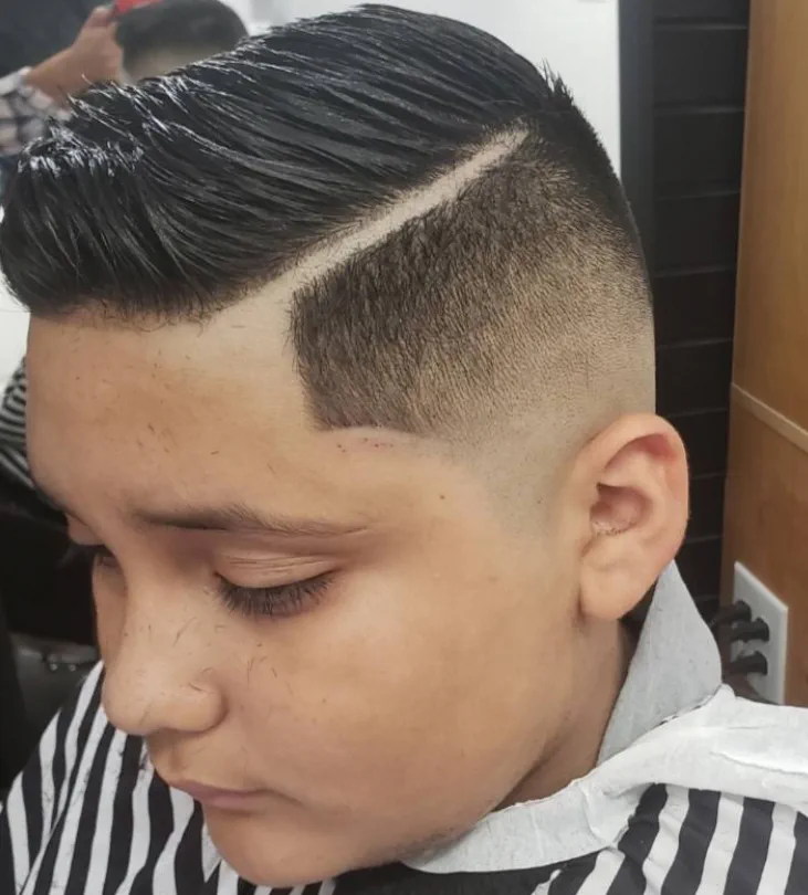 Boy's pompadour with a crisp hard part and clean fade.