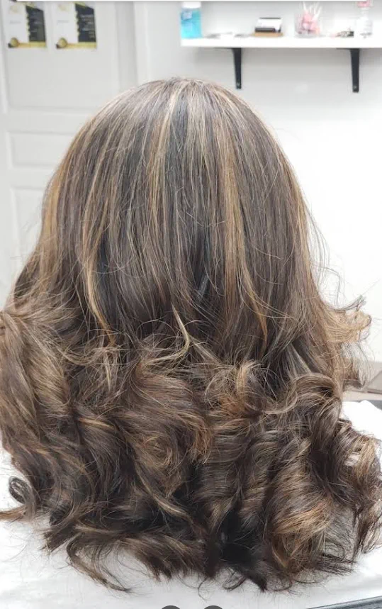 Dark hair with caramel highlights and soft curls.