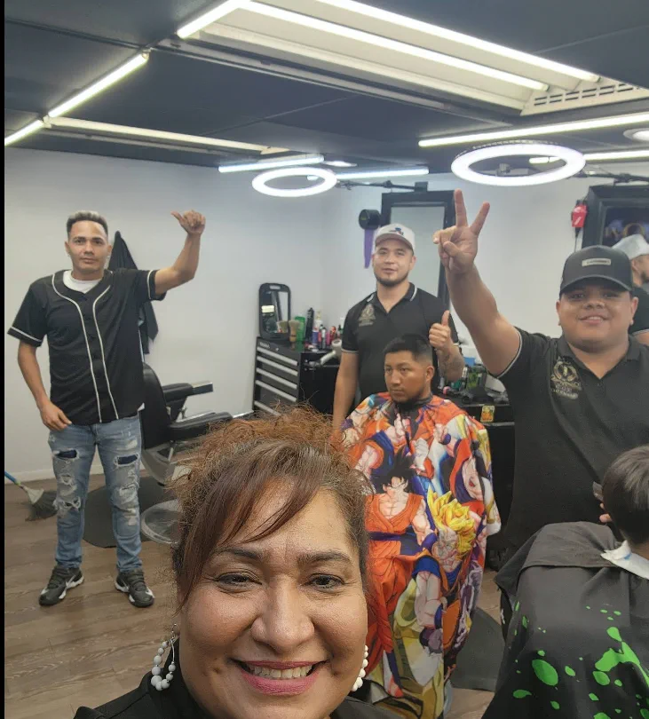 Angela, the owner, smiling up front with her barbers behind her in the shop.
